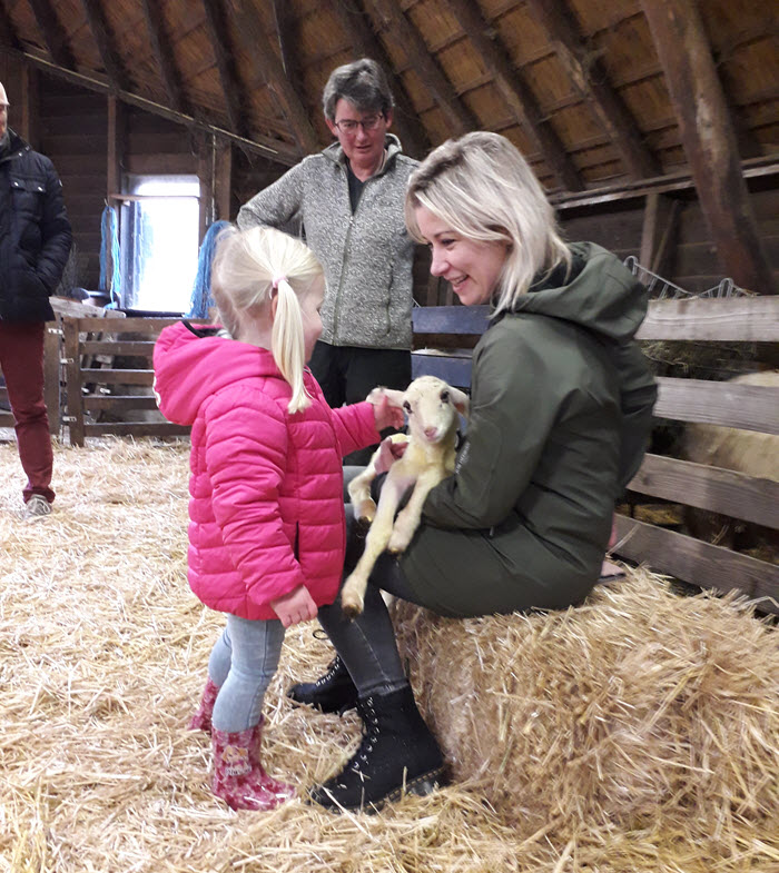 Carrie ten Napel met haar dochtertje met het eerste lammetje Max. Herder Marion Derks kijkt toe. 